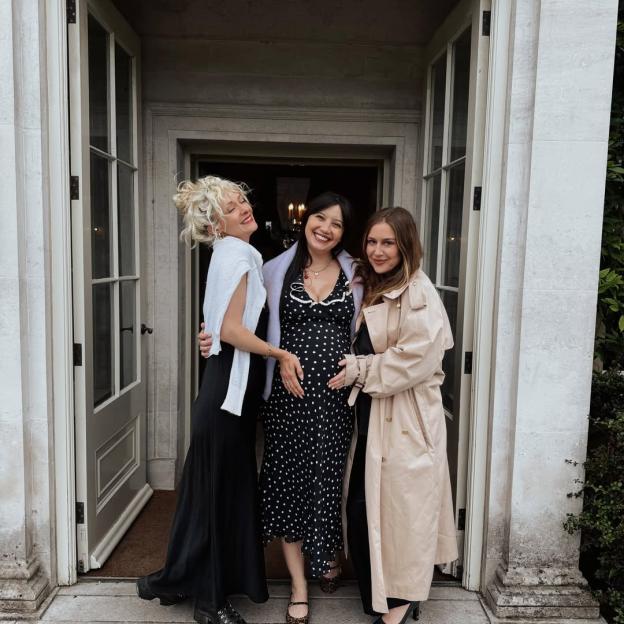 Three women, one pregnant, standing in a doorway smiling.