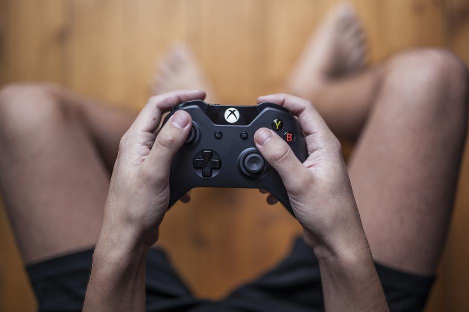 Hands holding an Xbox One controller while playing a video game.
