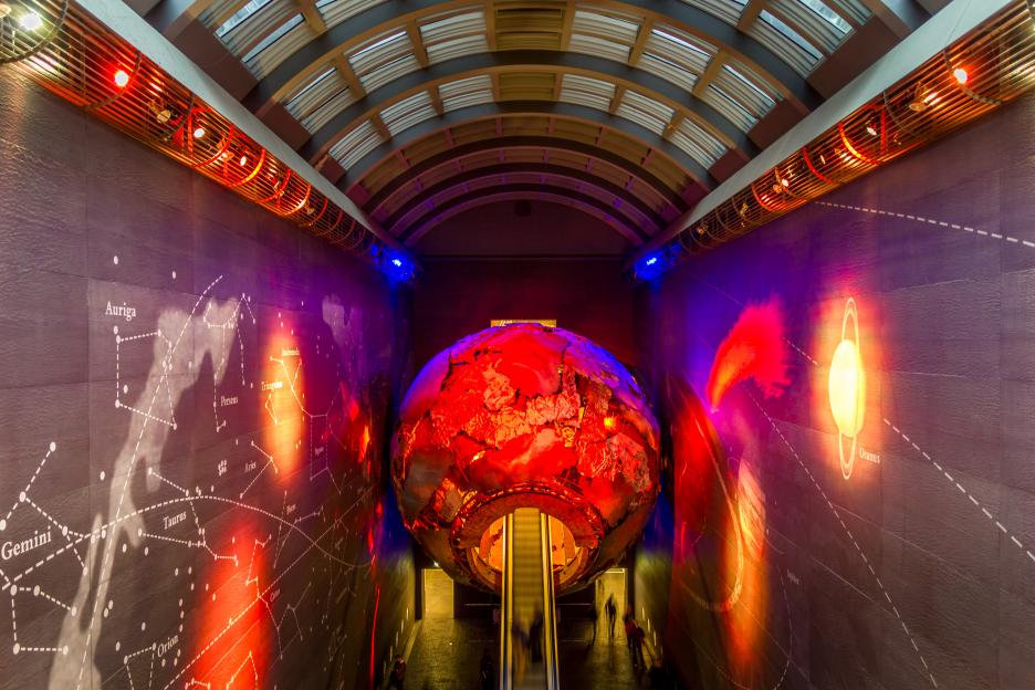 The Natural History Museum's Earth Hall with its large, red, textured globe at the center, flanked by walls with constellations and planets.