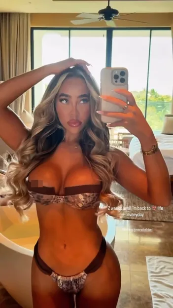 A woman in a patterned two-piece swimsuit takes a mirror selfie.