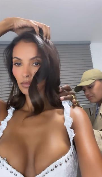 Maya Jama posing in a white top with another person adjusting her hair.
