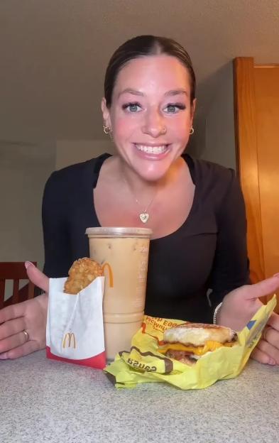 A woman smiles with a low-calorie McDonald's breakfast order of a hash brown, iced coffee, and breakfast sandwich.