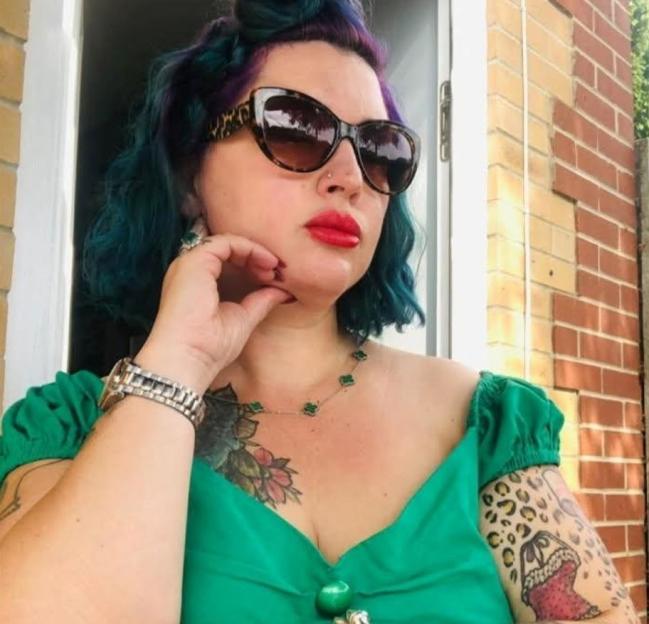 Tania Williams, a woman with blue hair, red lipstick, and sunglasses, looks to the right.