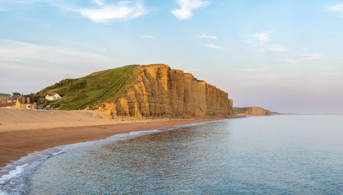 West Bay cliffs in Dorset, England, rising above a beach and calm sea.