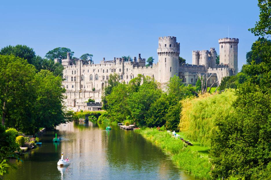 Warwick Castle by the River Avon on a clear day with two paddle boats.