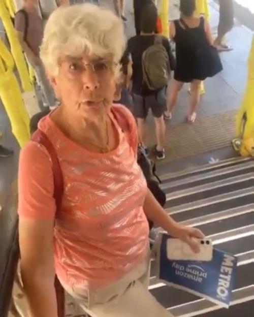 An older woman in a pink shirt and khaki shorts climbing stairs at a train station.