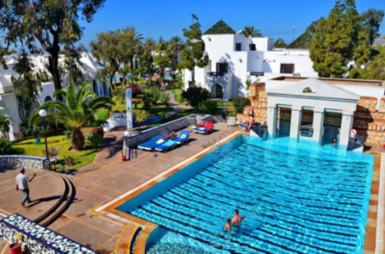 A resort with a large swimming pool, surrounded by white buildings and palm trees.