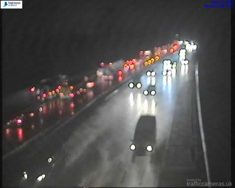 Nighttime view of heavy traffic on a wet highway with car headlights and taillights visible.