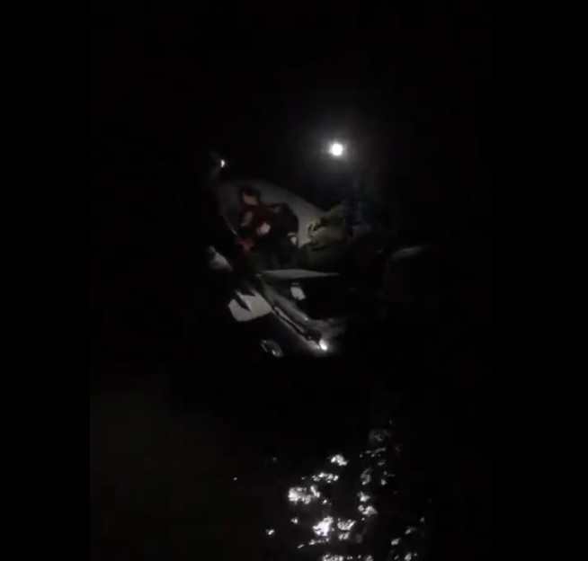 People in a boat on the water at night, illuminated by a headlamp.
