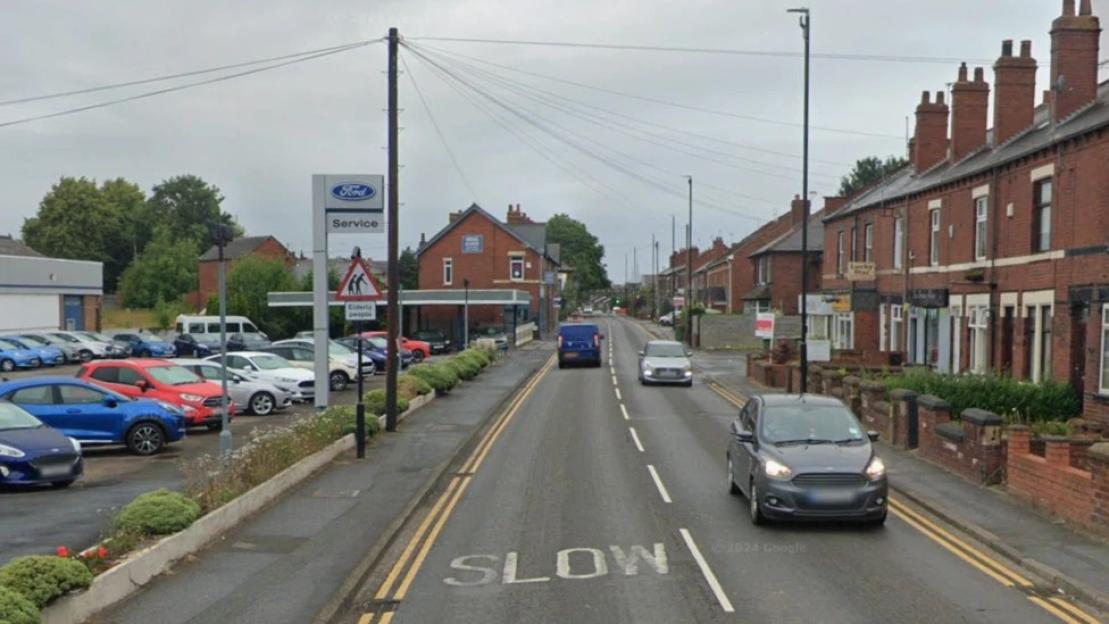 Street view of Aberford Road in Woodlesford with a Ford dealership on the left and residential brick houses on the right.