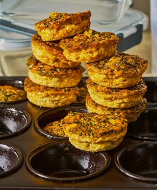 Spinach, feta, and sun-dried tomato egg breakfast muffins stacked in a muffin tin.