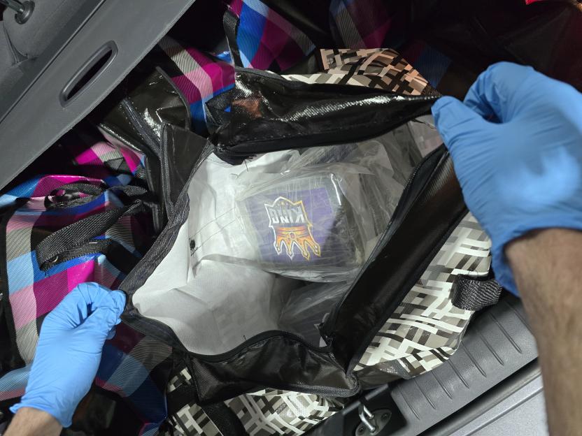 A person in blue gloves opening a large bag containing packaged Class A drugs.