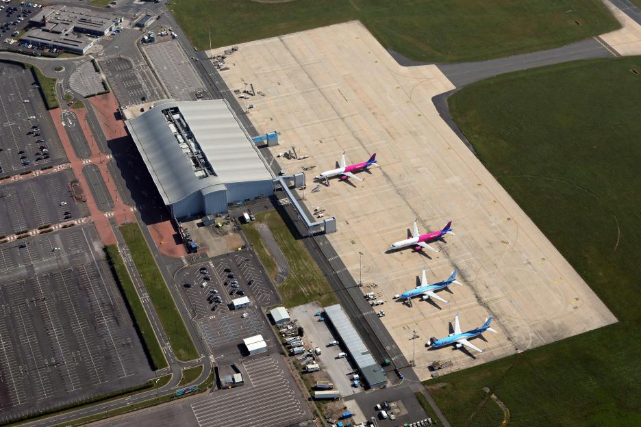 Aerial view of Doncaster Sheffield Airport with four passenger jets parked on the apron next to the terminal building and car parks.
