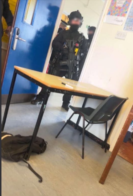 Armed police officers in full gear entering a school classroom.