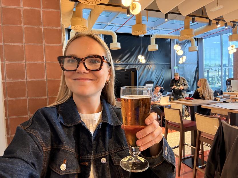A woman smiling while holding a glass of beer in a restaurant.