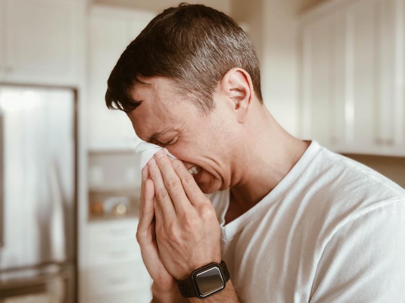 Man covering his nose and mouth with a tissue while sneezing.