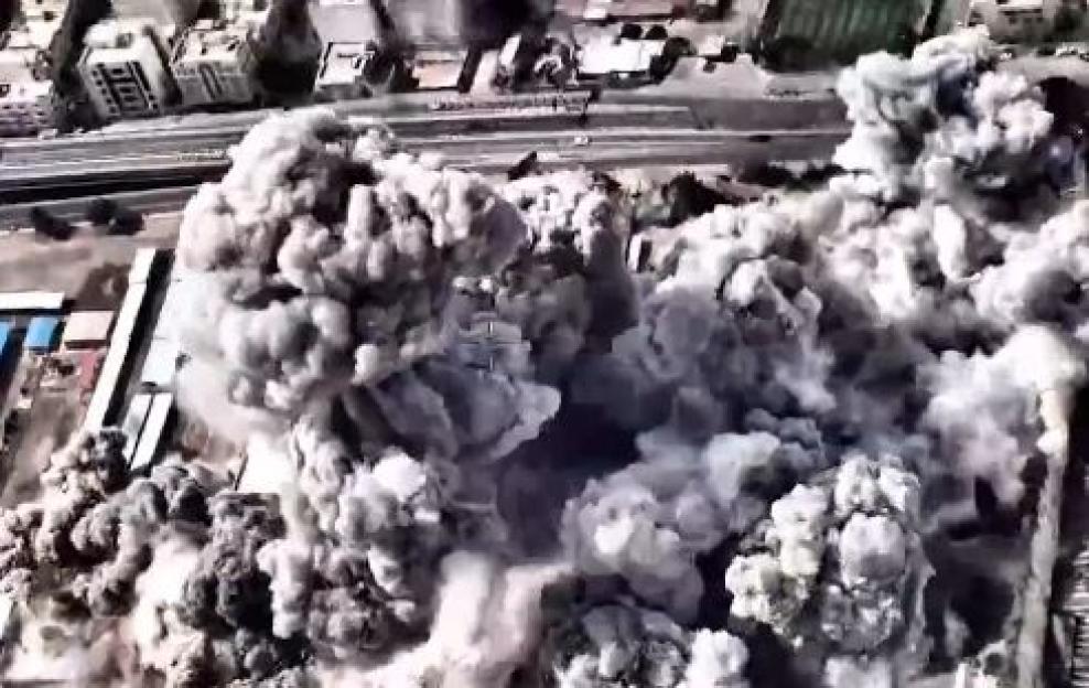 Aerial view of a large explosion with dense grey smoke billowing upwards from a city.
