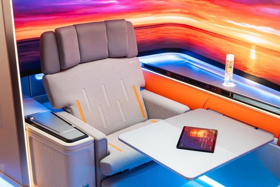 The Safran and RAVE Aerospace Origin concept cabin with a tablet on a table, a passenger seat, and an orange and pink lit background.