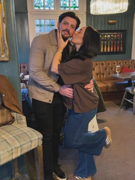 A woman kisses a man on the cheek inside a pub.