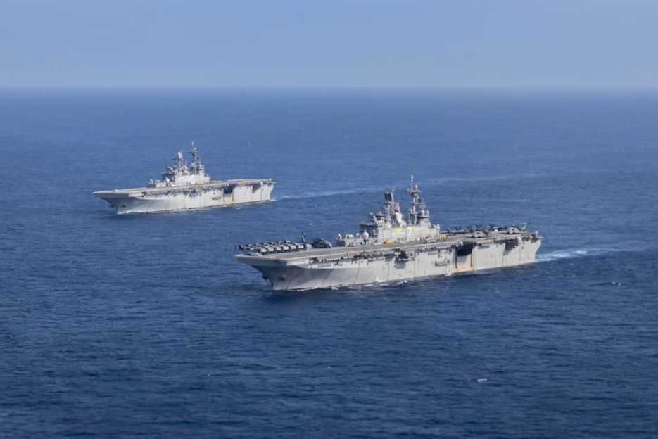 Two gray USS Tripoli ships sail in tandem on the blue ocean.