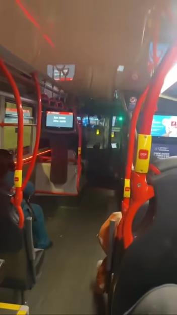 Inside a bus with red grab handles and screens displaying route information.