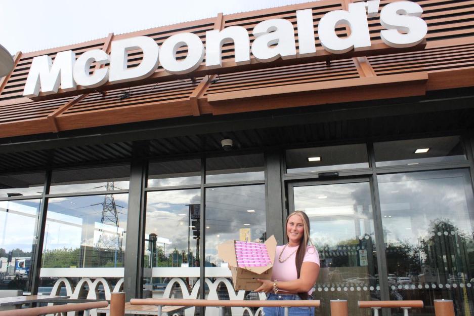 Sophie Sant holding a box of McDonald's curry sauce packets outside a McDonald's restaurant.