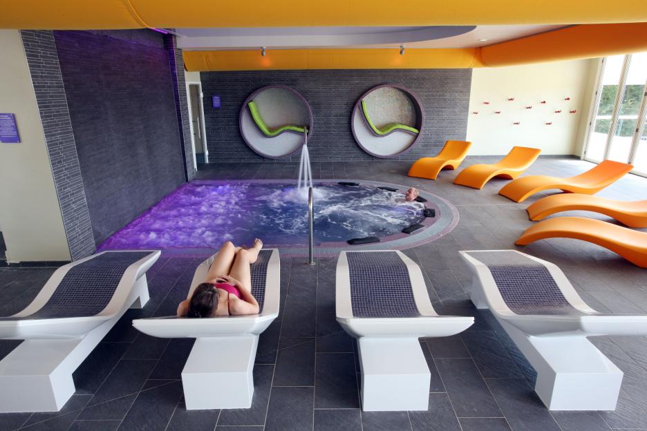 Butlins Ocean Hotel spa wet area with a woman relaxing on a sun lounger and a man in a hot tub.
