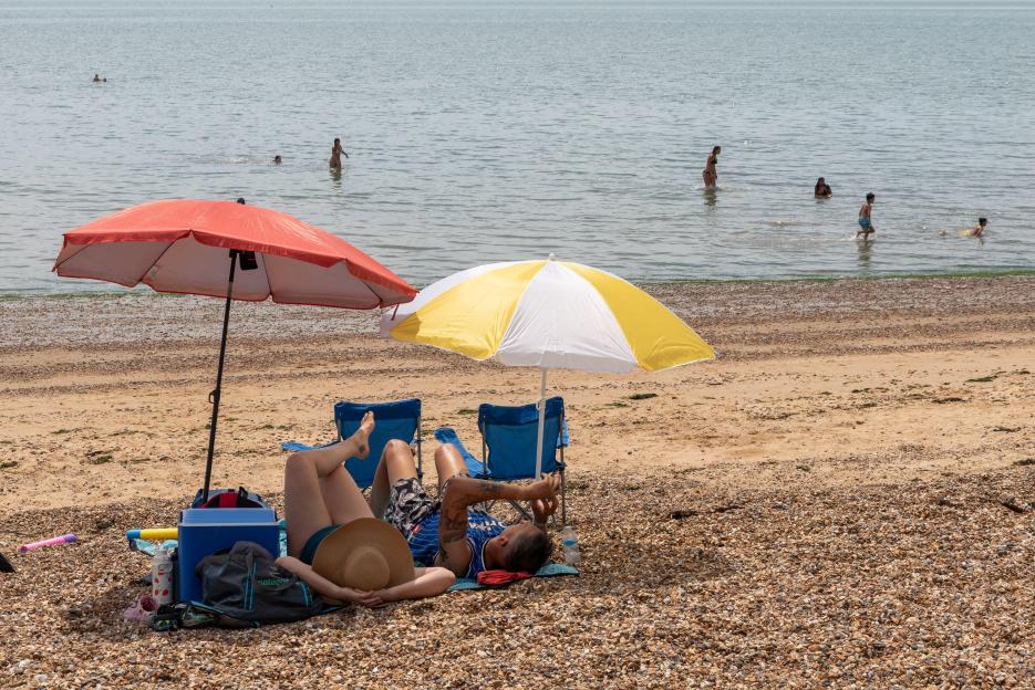 People relaxing on a beach under umbrellas with others swimming in the sea.