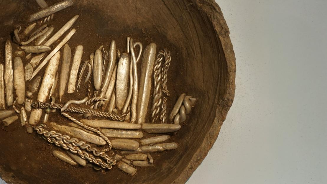 Viking Age silver hoard including bracelets, bars, and chains in a clay vessel.