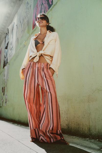 Woman wearing a tied-up shirt, bikini top, and striped wide-leg pants.