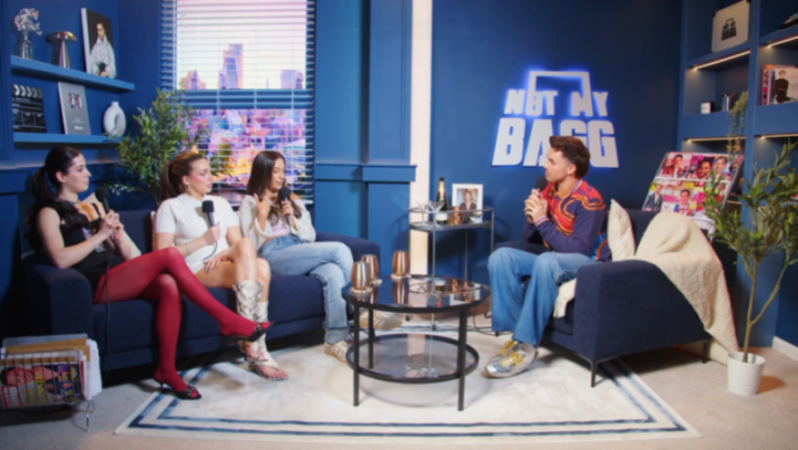 Four people sit on blue sofas in a studio with a "Not My Bagg" neon sign.