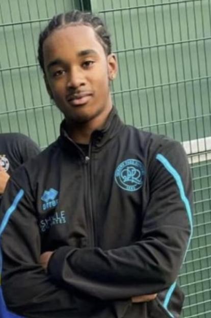 A young man in a black and blue tracksuit stands with his arms crossed.