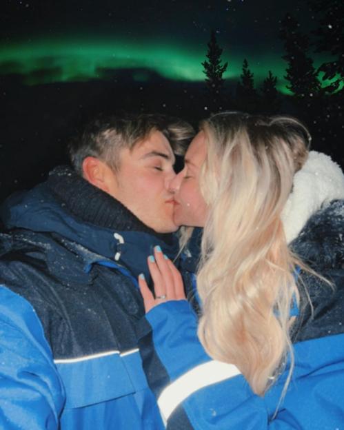 A couple kissing under the Northern Lights with snow falling.
