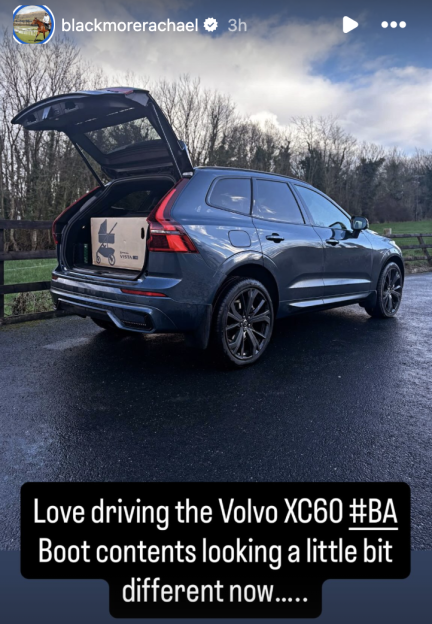 A dark blue Volvo XC60 with its trunk open, revealing a cardboard box containing a UPPAbaby Vista stroller.