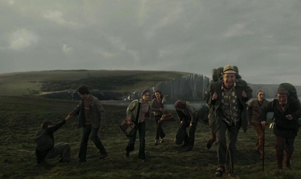 A group of people running across a grassy field with cliffs and water in the background.