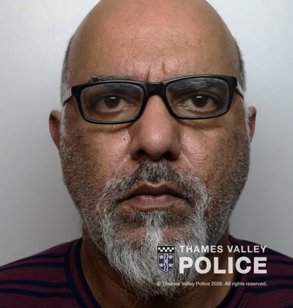 Mugshot of Amjad Ali, a bald man with a graying beard and glasses, wearing a striped shirt.