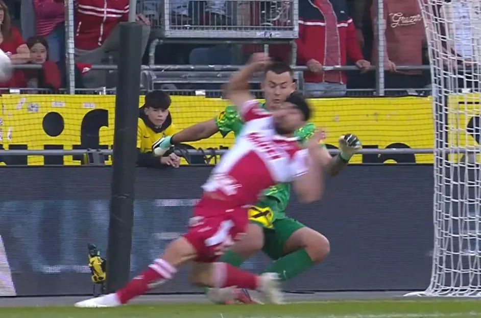 A goalkeeper suffers a leg injury during a football match, with his leg bending at an unnatural angle.