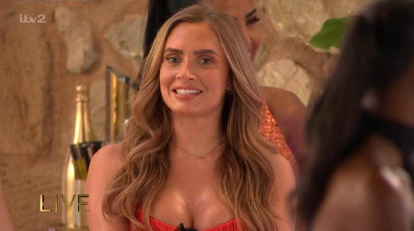 A young woman with long blonde hair smiles, wearing a red top.