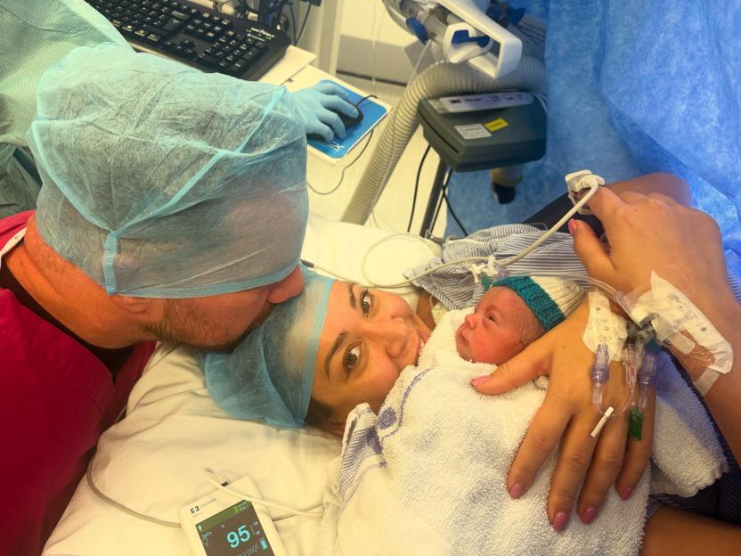 Jamie O'Hara kisses wife Keziah Grubb on the forehead as she holds their newborn daughter in a hospital bed.