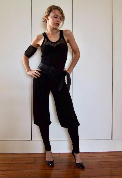 Kylie Minogue in an all-black outfit, with a fishnet top and arm band, posing for a video shoot.