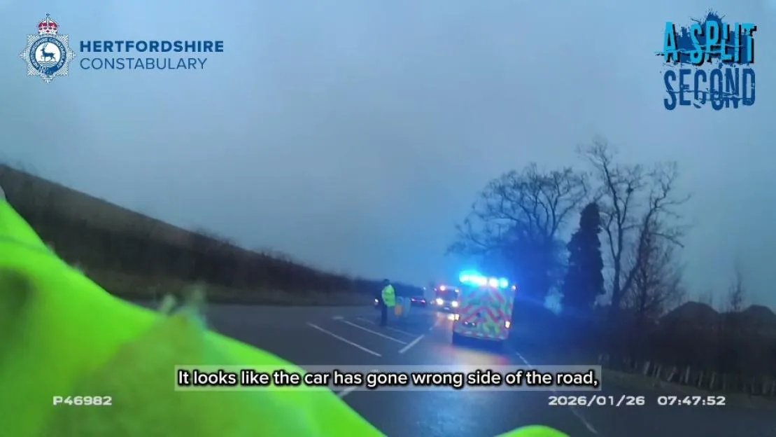 Dashcam footage from Hertfordshire Constabulary showing an emergency vehicle with flashing lights at a crash scene on a road.