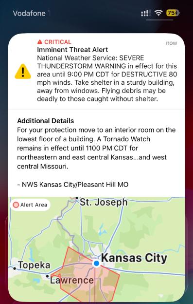 A phone screen showing an emergency alert for a severe thunderstorm and tornado watch in Kansas and Missouri, with a map highlighting the alert area, and a notification for a football watchalong.