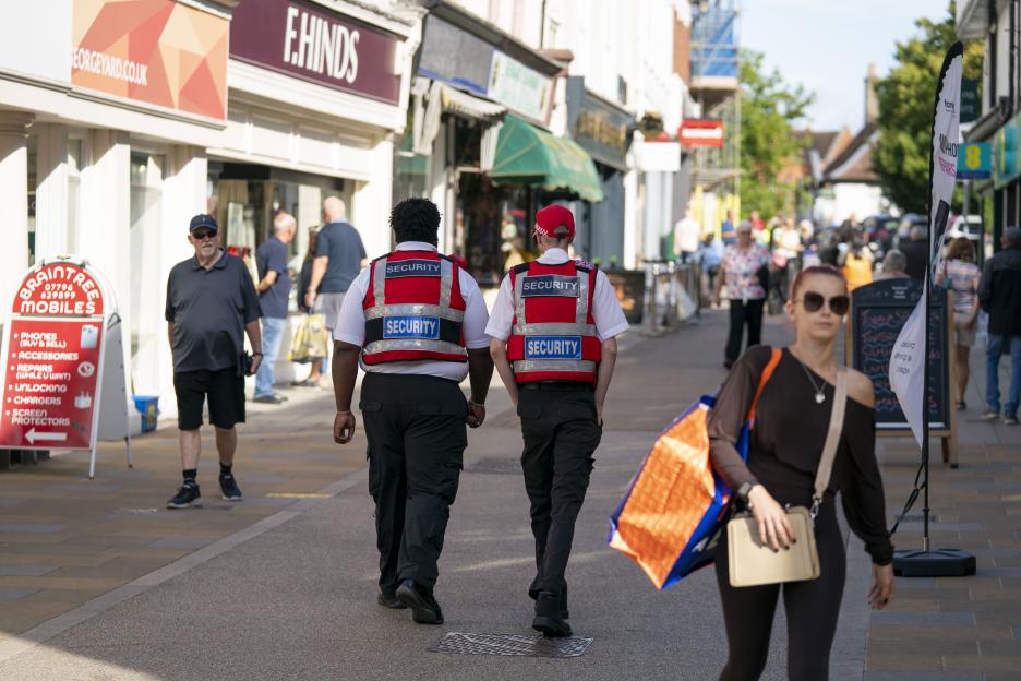 Two security guards in red vests patrolling a street in Braintree, Essex.