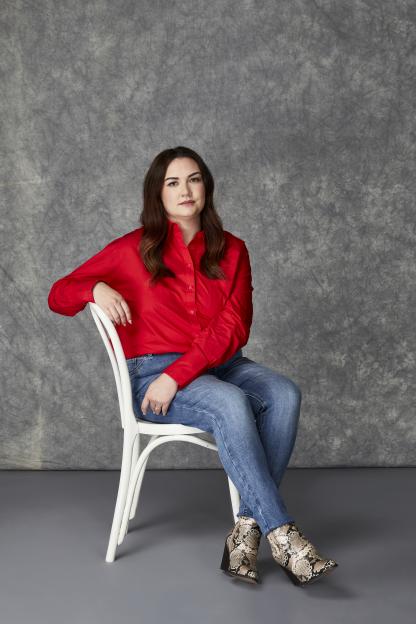 Lauren Eden Pen sitting on a chair, wearing a red shirt, blue jeans, and snakeskin boots.