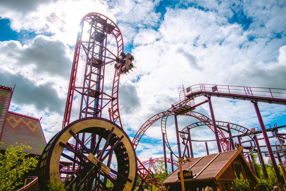 A roller coaster with a car of riders hanging upside down at the top of a loop, under a partly cloudy sky.