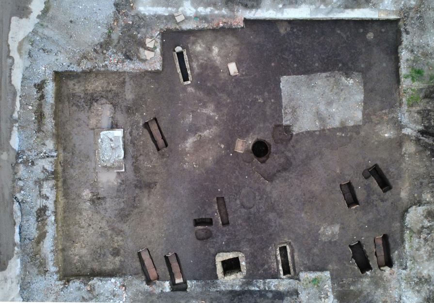 Aerial view of an archaeological excavation site showing several rectangular burial pits and one round pit.