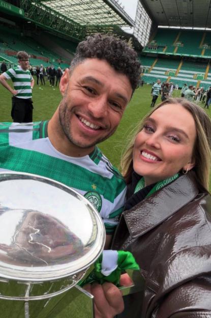 A man in a green and white striped shirt and a woman in a brown jacket holding a silver trophy in a stadium.
