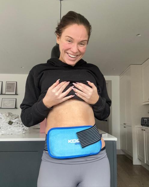 Vicky Pattison smiling while lifting her top to reveal an ice pack wrapped around her midsection.