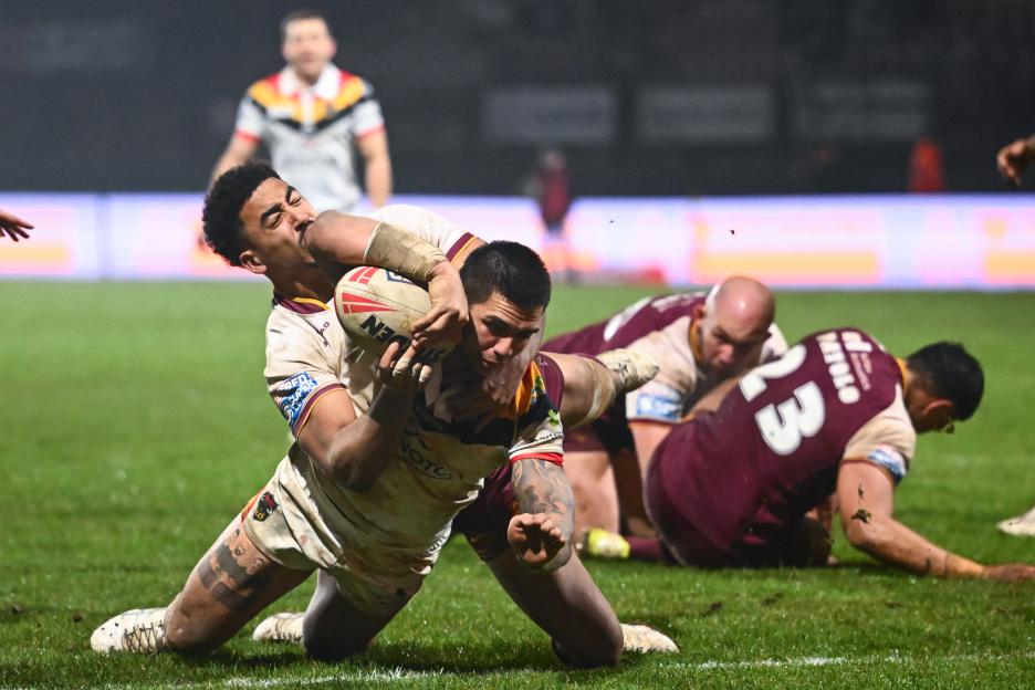 Nikorima of Huddersfield Giants scores a try while being tackled by a Bradford Bulls player.