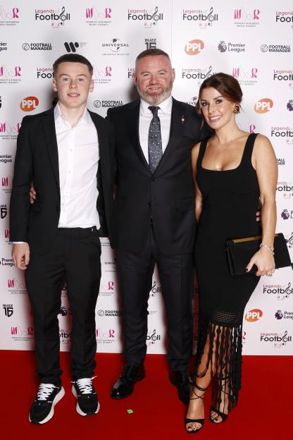 Kai Rooney, Wayne Rooney, and Coleen Rooney pose together on a red carpet.